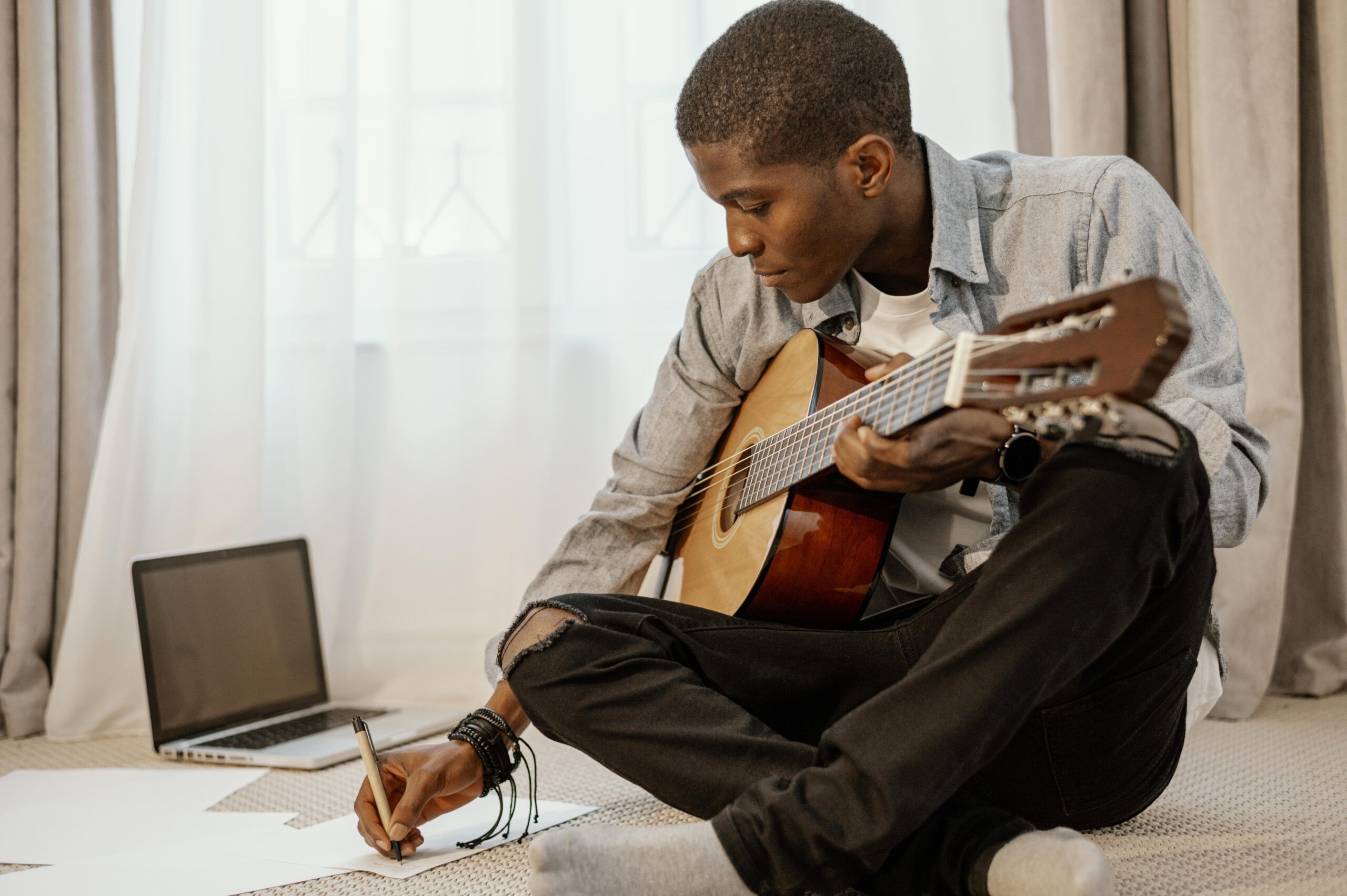 front-view-male-musician-writing-music-with-guitar-bed-laptop